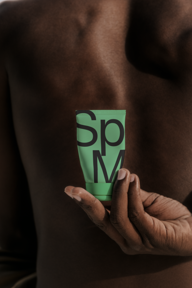 Person holding a green lotion tube with "Sp" text mockup, ideal for beauty product branding, packaging design, and advertising graphics.